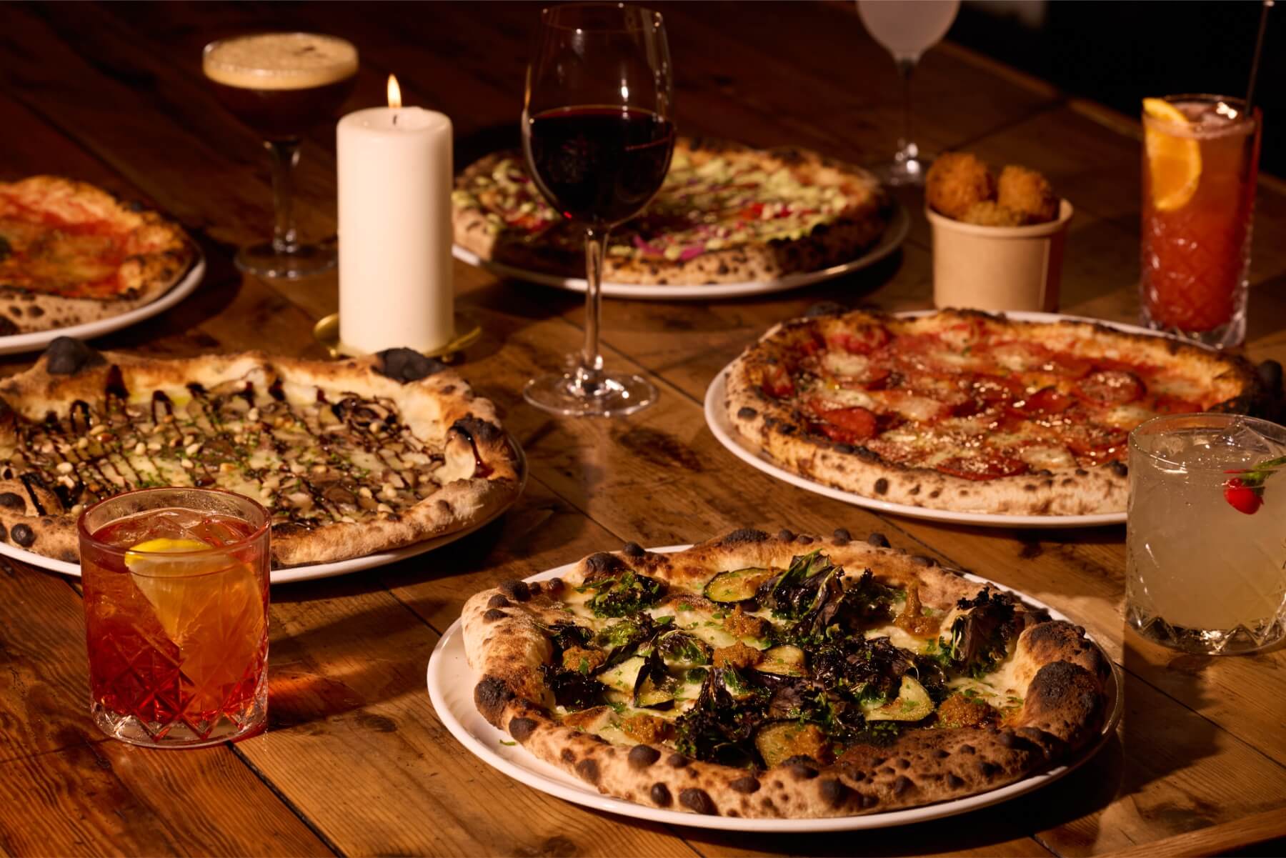 Candles, pizzas, red wine and cocktails on a table